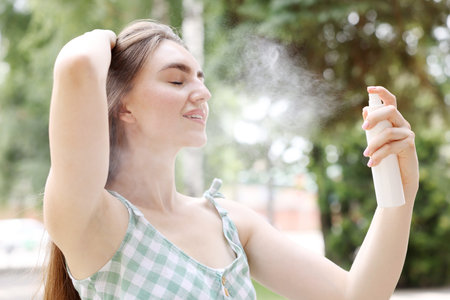 Smiling woman spraying thermal water onto her face outdoors