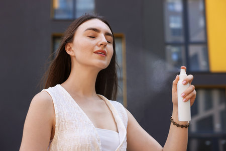 Smiling woman spraying thermal water from bottle outdoorsの写真素材