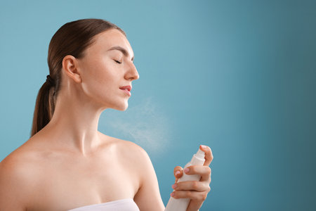 Beautiful woman spraying thermal water onto her neck on light blue background. Space for textの写真素材
