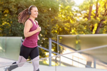 Athletic young woman with headphones in sportswear running outdoors, space for textの写真素材
