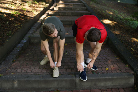 Young man and professional personal trainer tying shoes outdoors