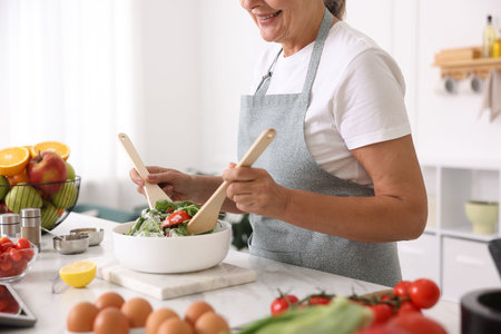 Senior woman cooking salad at white marble table in kitchen, closeupの写真素材