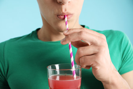 Man drinking juice through straw on light blue background, closeupの写真素材