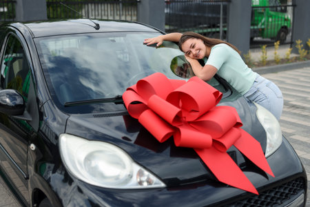 Dreams come true. Woman near her new auto with big red bow outdoors