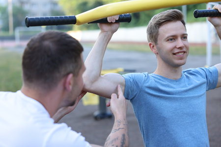 Young man exercising with outdoor gym equipment with professional personal trainer outdoorsの写真素材