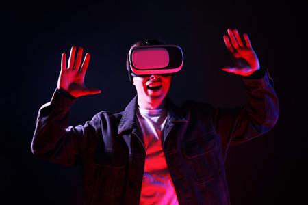 Emotional man using virtual reality headset in neon lights against black backgroundの写真素材