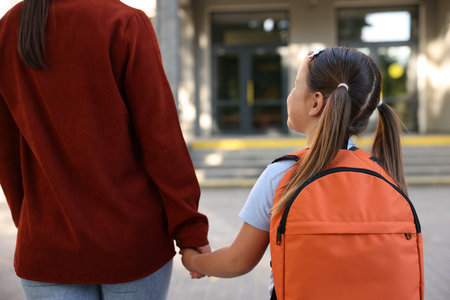 Mother taking her daughter to school outdoors, back viewの写真素材