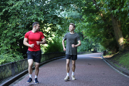 Young man running with professional personal trainer outdoors. Space for text