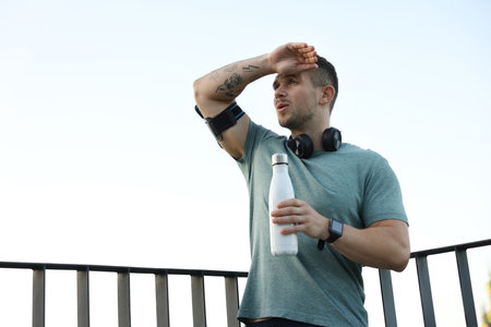 Athletic young man in sportswear with bottle of water before running outdoors, low angle viewの写真素材