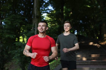 Young man running with professional personal trainer outdoorsの写真素材