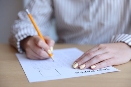Student filling out multiple choice test at table, closeup. Passing exam