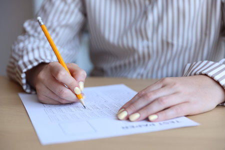 Student filling out multiple choice test at table, closeup. Passing examの写真素材