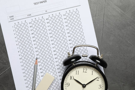 Answer sheet, alarm clock, pencil and eraser on gray textured table, flat lay. Student passing examの写真素材