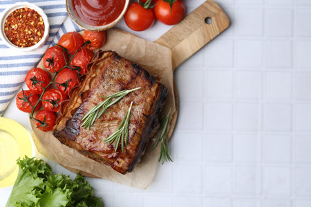 Delicious roast beef with rosemary, tomatoes and other products on white tiled table, flat lay....