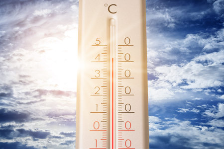 High temperature on thermometer against blue sky on sunny day. Summer weather
