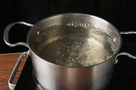 Metal pot with boiling water on stove in kitchen, closeupの写真素材