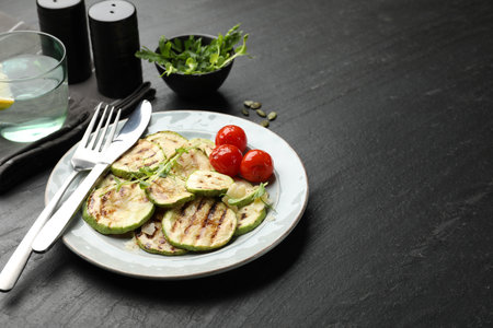 Delicious grilled courgette slices with tomatoes and microgreens served on black textured table, closeupの写真素材
