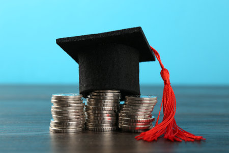 Scholarship. Graduate hat and coins on wooden table against light blue background, closeupの写真素材
