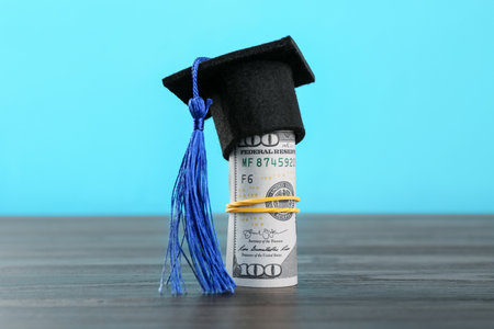 Scholarship. Graduate hat and dollar banknotes on wooden table against light blue background, closeupの写真素材