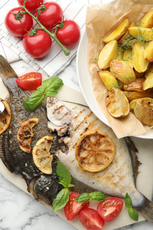 Tasty roasted flounder fish served with potatoes, tomatoes, basil and lemon slices on white marble table, flat lay. Homemade seafood dishの写真素材