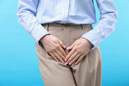 Woman suffering from cystitis symptoms on light blue background, closeup