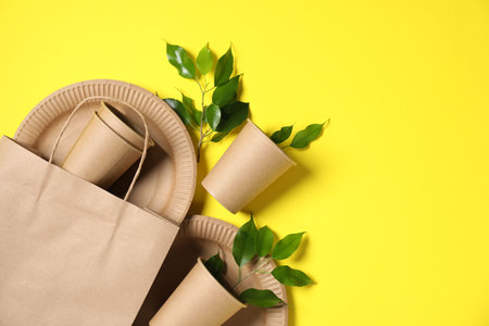Different eco friendly packaging, tableware and leaves on yellow background, flat lay. Space for textの写真素材