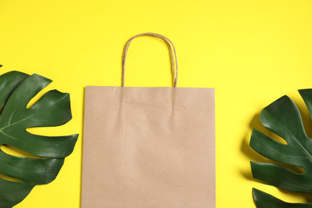 Eco friendly packaging. One paper bag and leaves on yellow background, flat layの写真素材