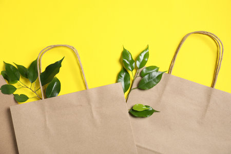 Eco friendly packaging. Paper bags and leaves on yellow background, flat layの写真素材