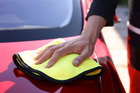 Man wiping car hood with yellow microfiber rag outdoors, closeupの写真素材