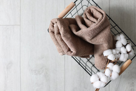 Clean towels and cotton flowers in metal basket on light wooden floor, top view. Space for textの写真素材
