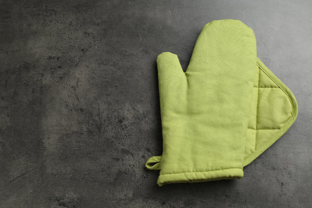 Green oven glove and potholder on dark textured table, top view. Space for textの写真素材