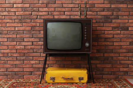Retro TV on stand, suitcase and carpet near red brick wall. Used stuffの写真素材
