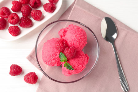 Delicious raspberry sorbet with mint in bowl, spoon and fresh berries on white wooden table, flat layの写真素材