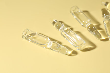 Glass ampoules with liquid on yellow background, flat lay