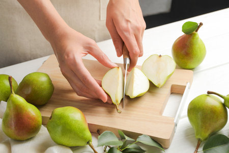 Woman cutting fresh ripe pear at white wooden table, closeupの写真素材