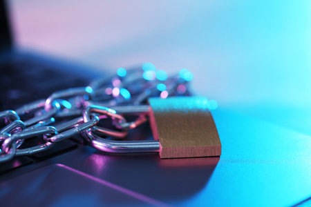 Cyber safety. Metal padlock with chain and laptop on table, closeupの写真素材