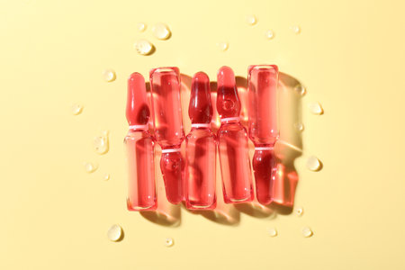 Glass ampoules with liquid and water drops on yellow background, flat layの写真素材
