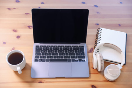Home workspace. Laptop, cup of tea, notebook and headphones on wooden desk, above view
