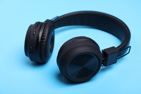 Pair of stylish black headphones on light blue background, closeup