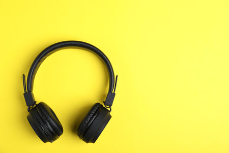 Pair of stylish black headphones on yellow background, top view. Space for textの写真素材