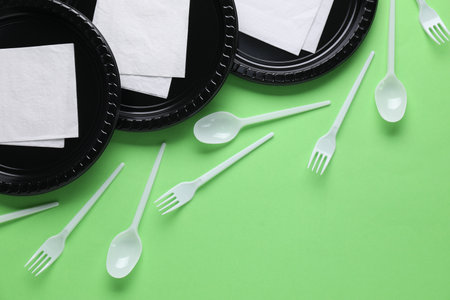 Set of disposable plastic tableware and paper napkins on green background, flat layの写真素材