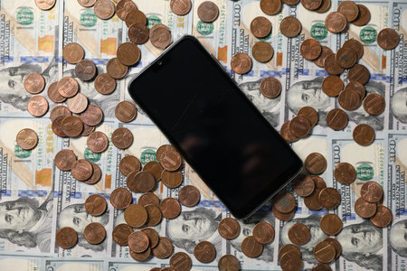 Smartphone and coins on dollar banknotes as background, top viewの写真素材