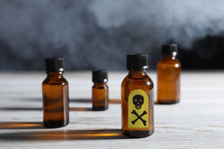 Bottles of poisons with warning sign on wooden table against dark background with smoke, closeupの写真素材
