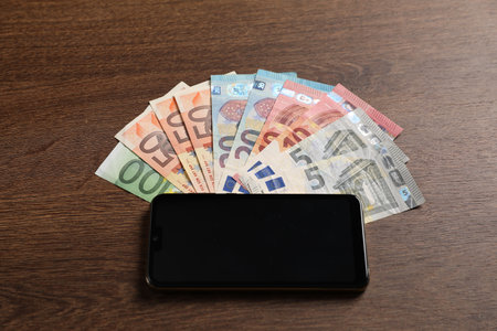 Smartphone and euro banknotes on wooden table, above viewの写真素材