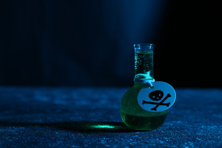 Flask of poison with warning sign on textured table against dark background, closeup. Space for text