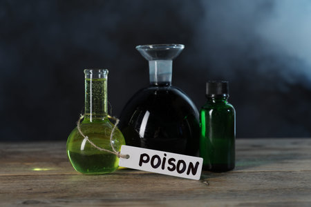 Bottles with poisons on wooden table against dark background with smokeの写真素材