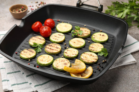 Delicious grilled courgette slices with tomatoes, lemon and parsley in pan on grey textured table, closeupの写真素材