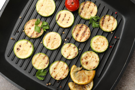 Delicious grilled courgette slices with tomatoes, lemon and parsley in pan on grey textured table, top viewの写真素材