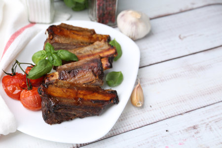 Roasted beef ribs, tomatoes and spices on white wooden table, closeup. Space for textの写真素材
