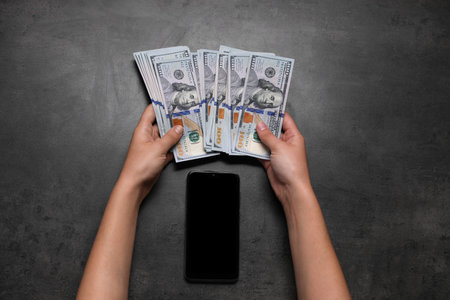 Woman with money and smartphone at grey table, top view